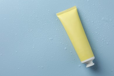 Photo of Moisturizing cream in tube on light blue background with water drops, top view. Space for text