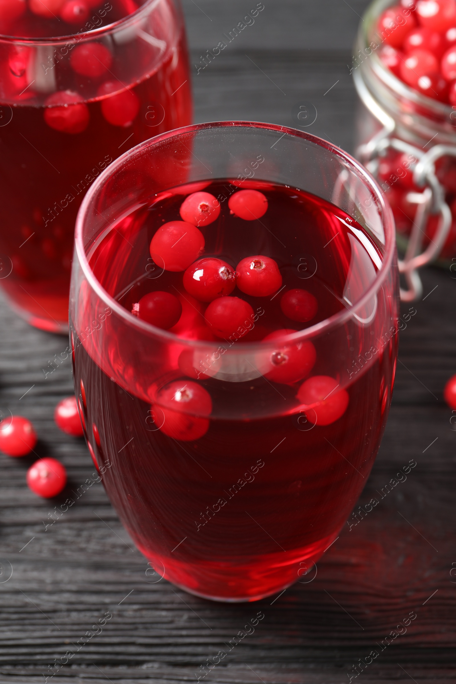 Photo of Tasty cranberry juice in glasses and fresh berries on black wooden table, closeup