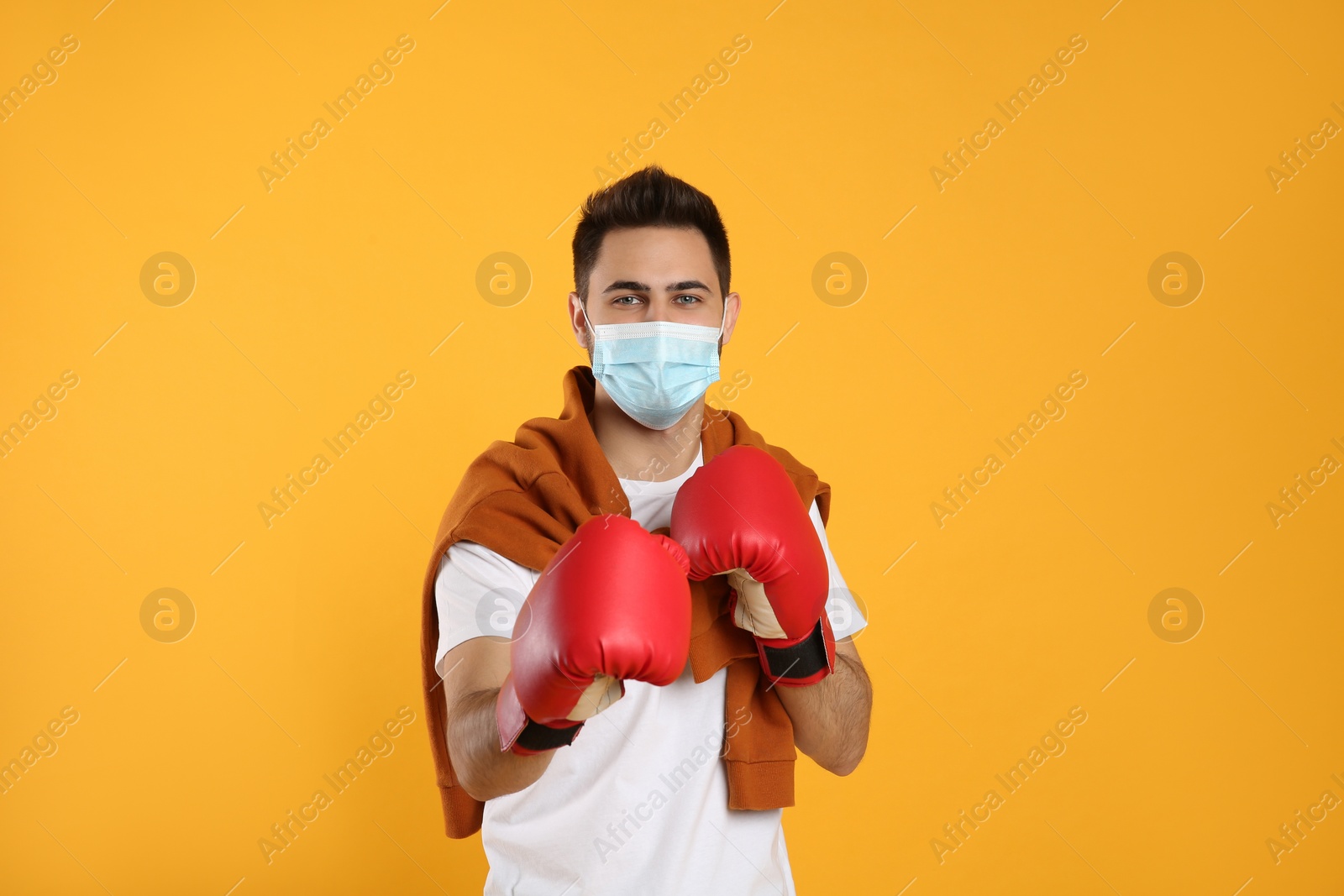 Photo of Man with protective mask and boxing gloves on yellow background. Strong immunity concept