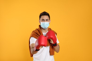 Photo of Man with protective mask and boxing gloves on yellow background. Strong immunity concept