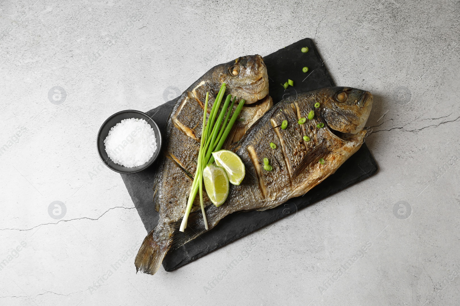 Photo of Seafood. Delicious baked fish served with green onion and lime on light textured table, top view