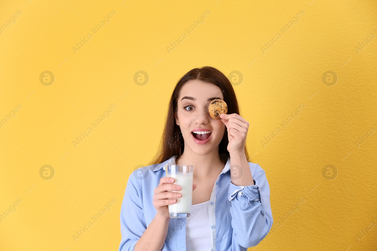 Photo of Beautiful young woman drinking milk with cookie on color background