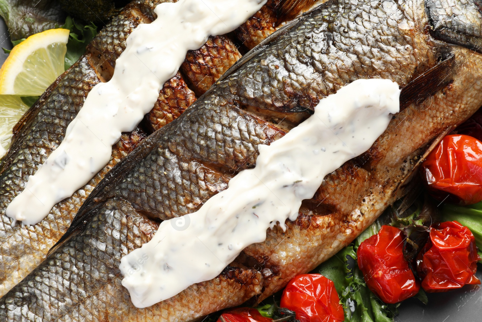 Photo of Delicious baked sea bass fish with sauce on plate, closeup