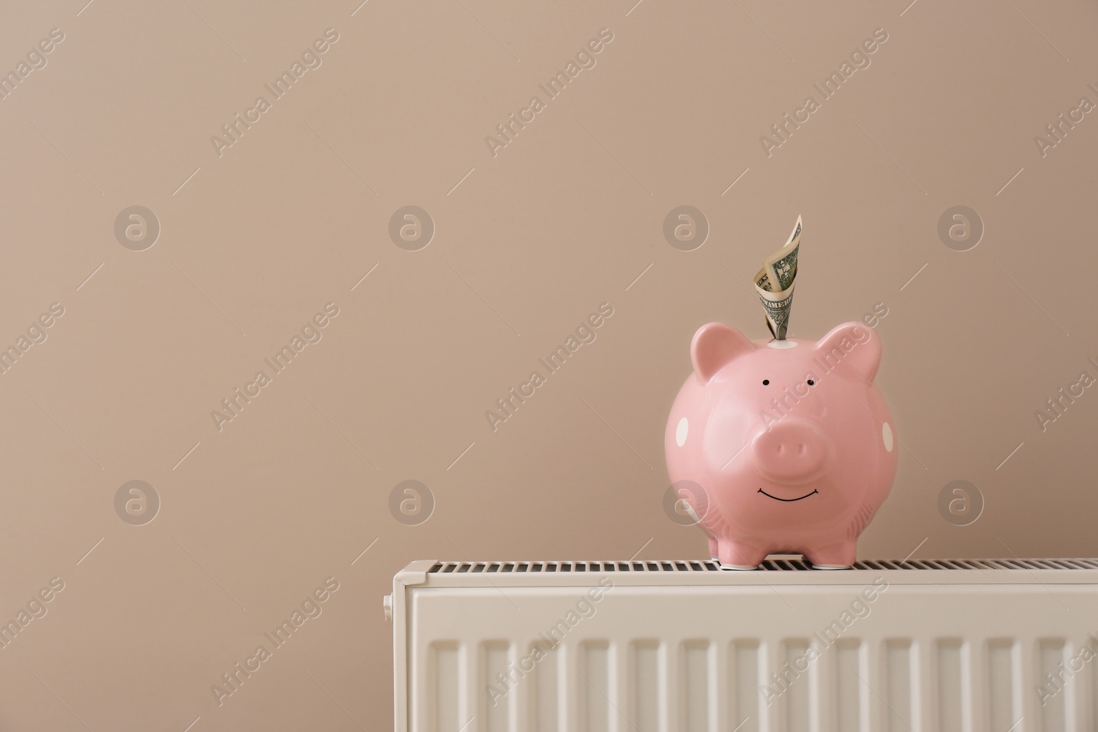 Photo of Heating radiator with piggy bank and money near color wall. Space for text