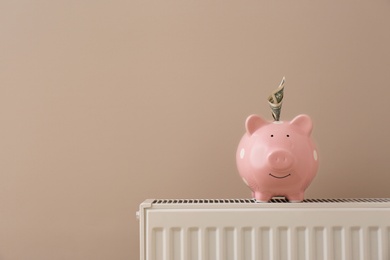 Heating radiator with piggy bank and money near color wall. Space for text