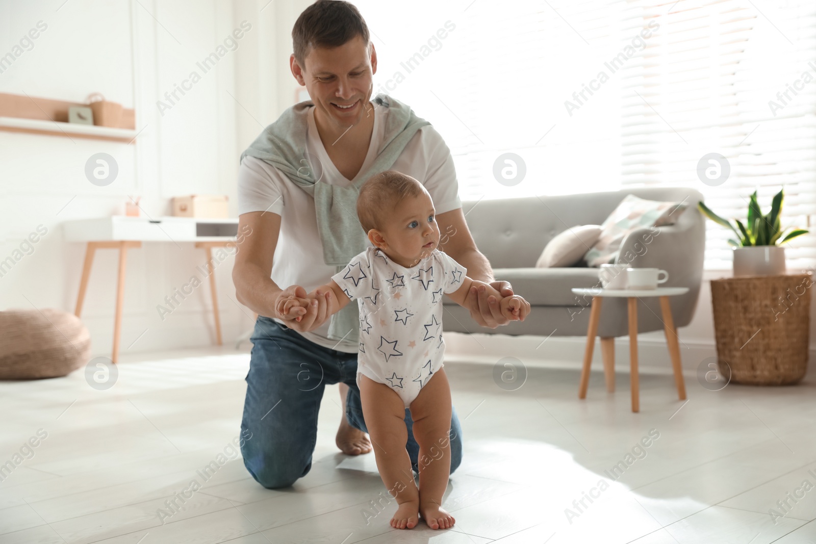 Photo of Father supporting his baby daughter while she learning to walk at home