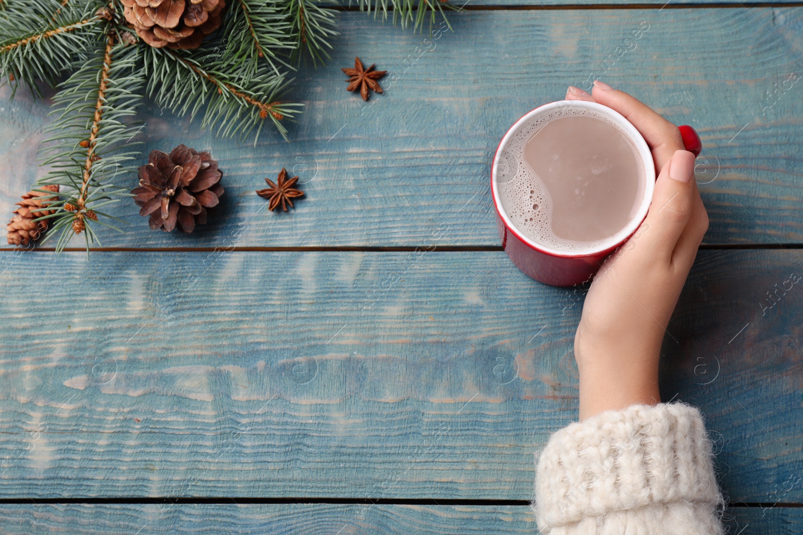 Photo of Woman holding cup of tasty cocoa on blue wooden table, top view. Space for text