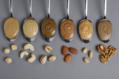 Tasty nut butters in spoons and raw nuts on gray table, flat lay