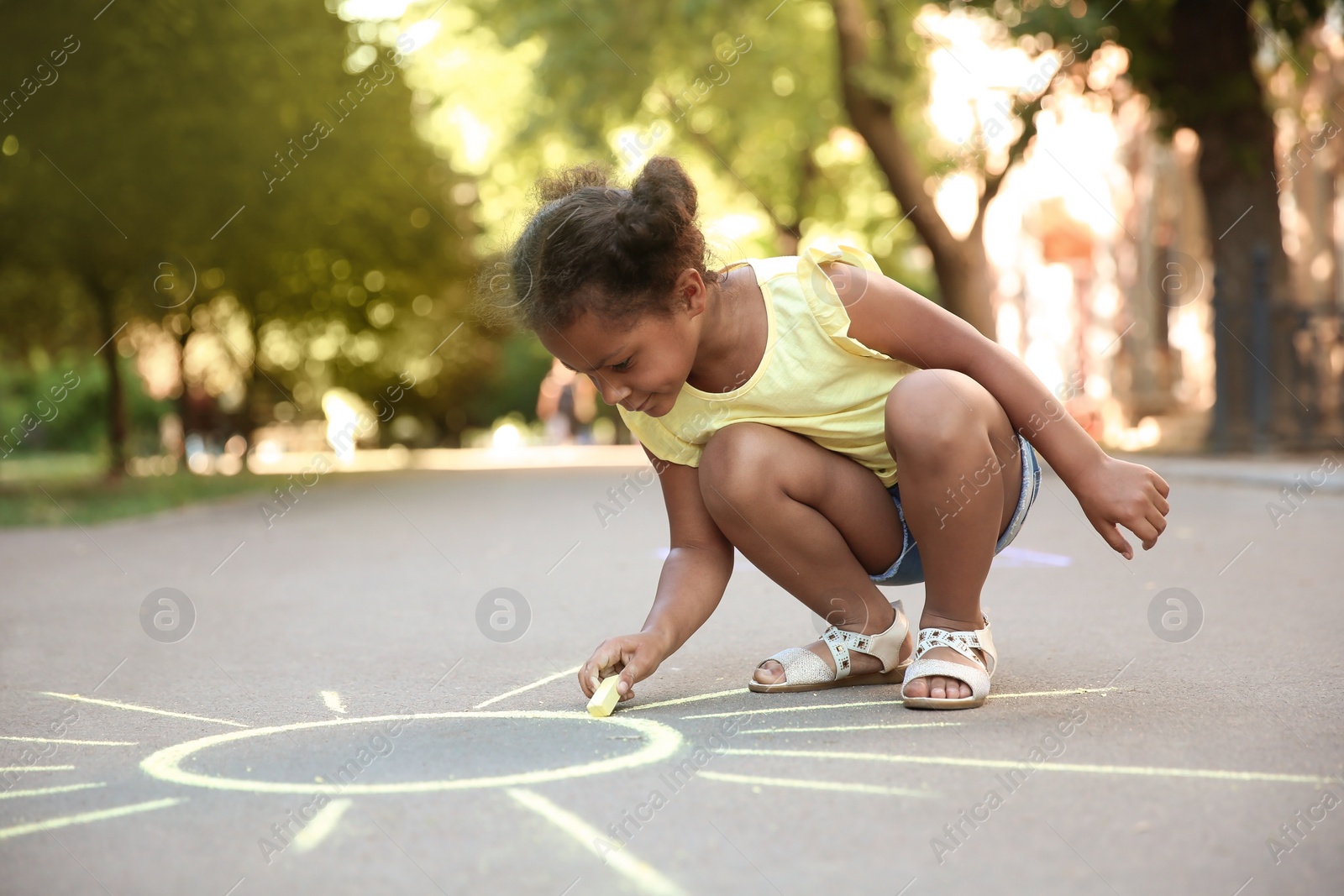 Photo of Little African-American child drawing sun with chalk on asphalt