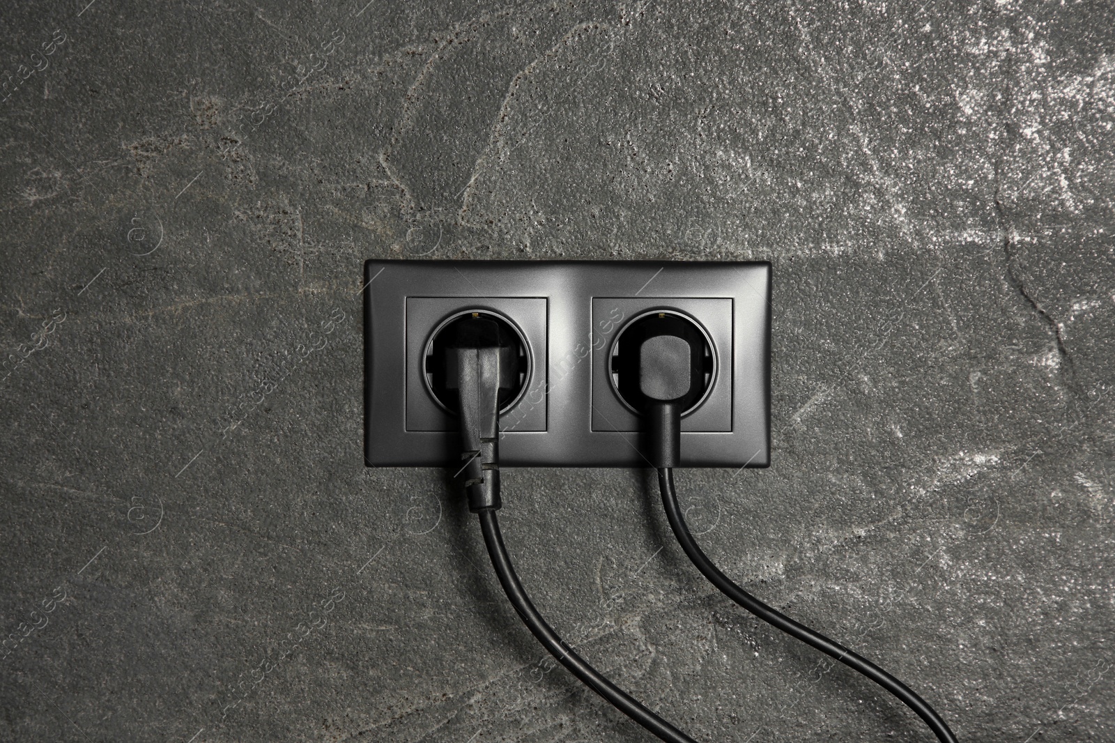 Photo of Power sockets with inserted plugs on dark grey wall. Electrical supply