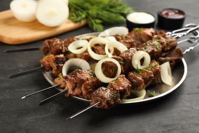 Photo of Metal skewers with delicious meat and onion served on black table
