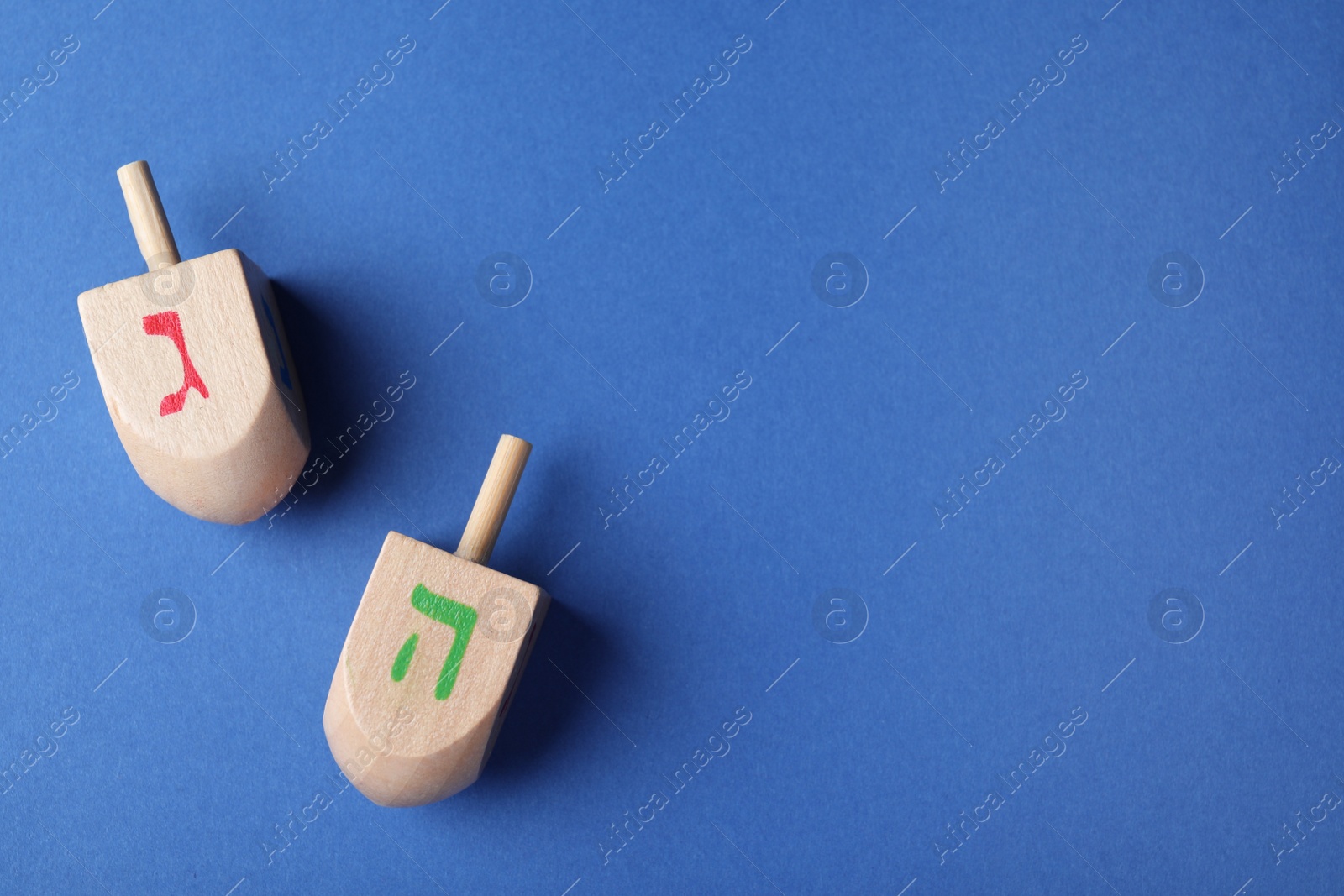 Photo of Hanukkah traditional dreidels with letters Gimel and He on blue background, flat lay. Space for text