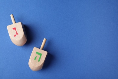 Photo of Hanukkah traditional dreidels with letters Gimel and He on blue background, flat lay. Space for text