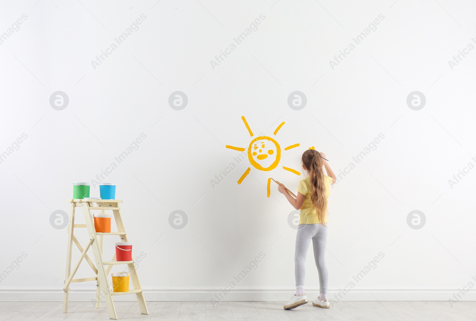 Photo of Little child painting sun on white wall indoors