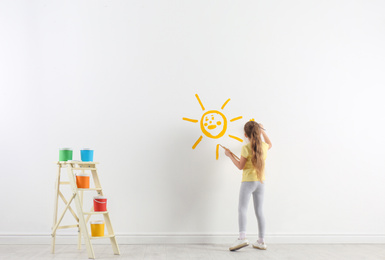 Photo of Little child painting sun on white wall indoors