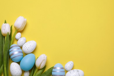 Photo of Flat lay composition of painted Easter eggs and tulip flowers on yellow background. Space for text