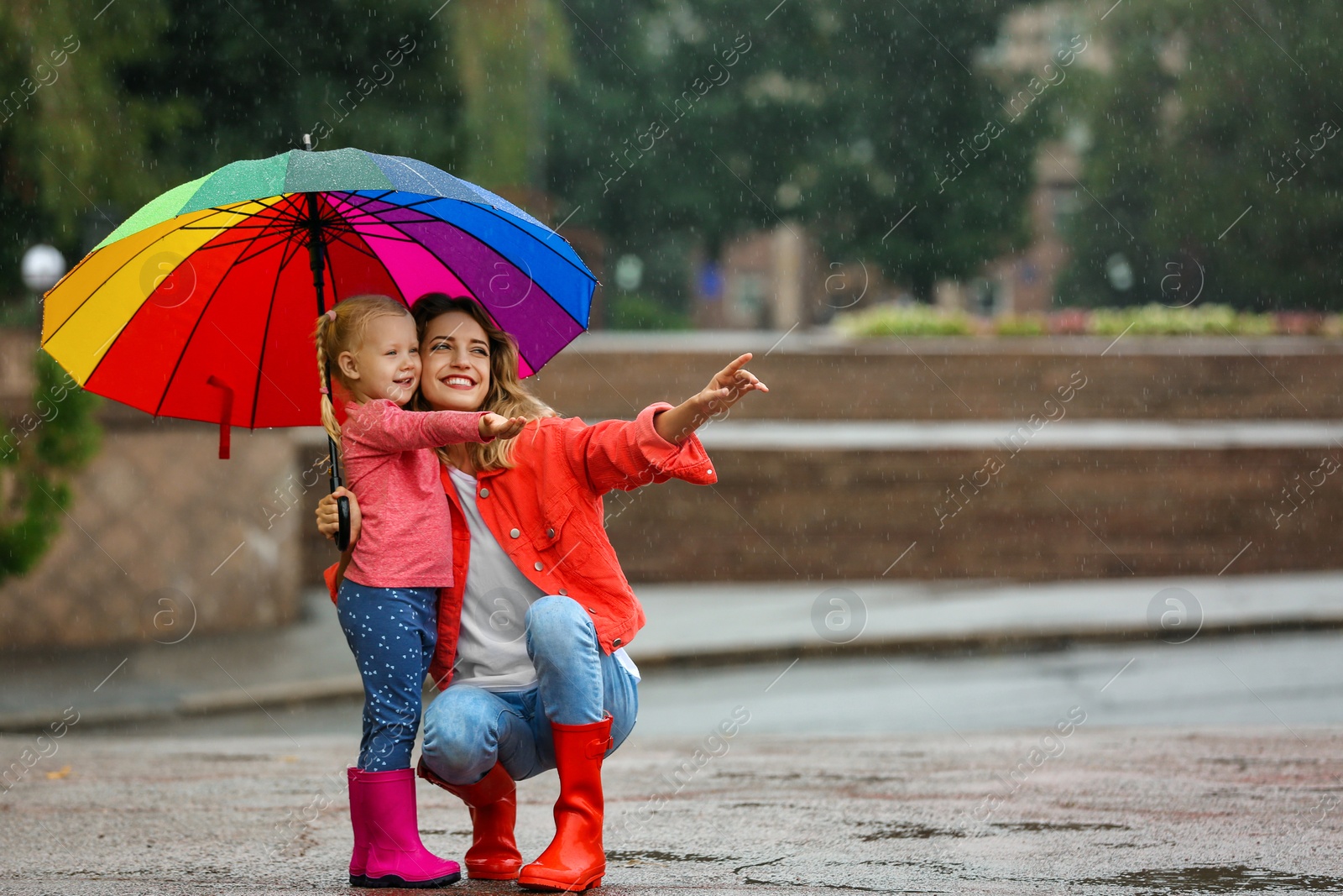 Photo of Happy mother and daughter with bright umbrella under rain outdoors