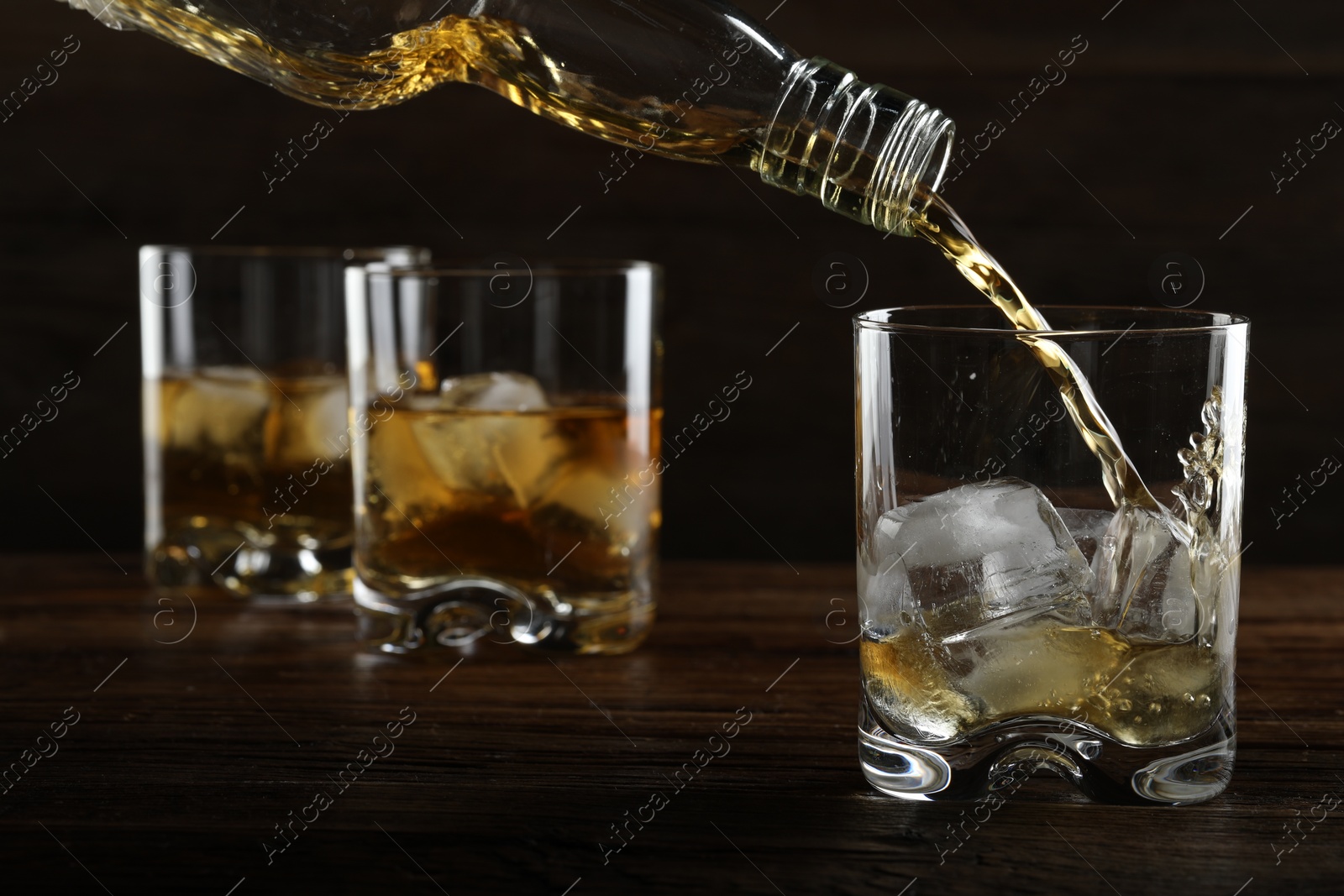 Photo of Pouring whiskey from bottle into glass at wooden table, closeup