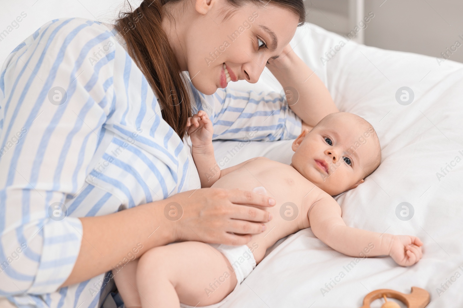 Photo of Happy young woman applying body cream onto baby`s skin on bed