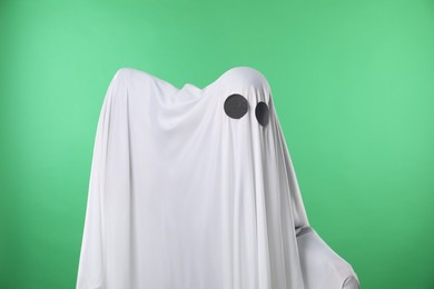 Photo of Creepy ghost. Person covered with white sheet on green background