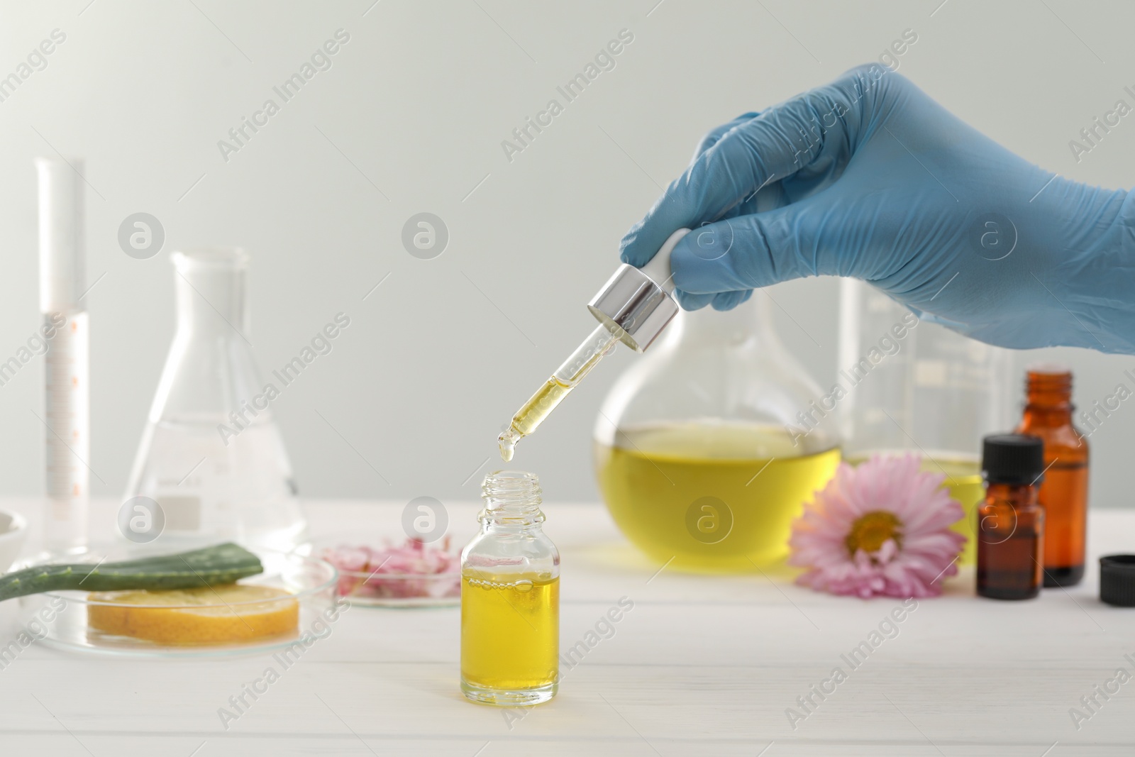 Photo of Scientist developing cosmetic oil at white table, closeup