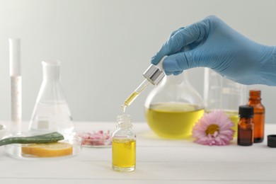 Photo of Scientist developing cosmetic oil at white table, closeup