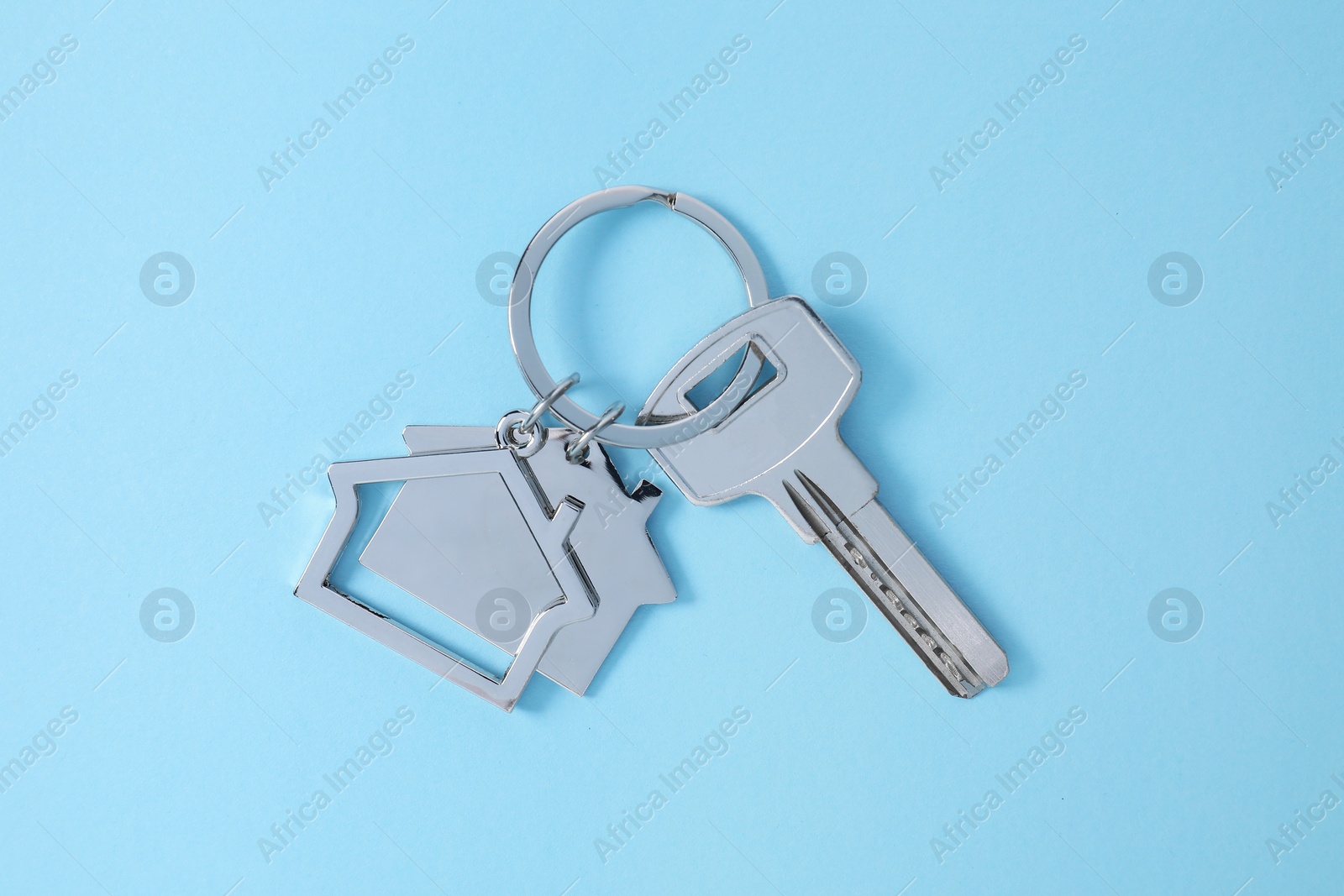 Photo of Key with keychain in shape of house on light blue background, top view