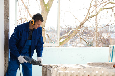 Photo of Worker using rotary drill hammer for window installation indoors