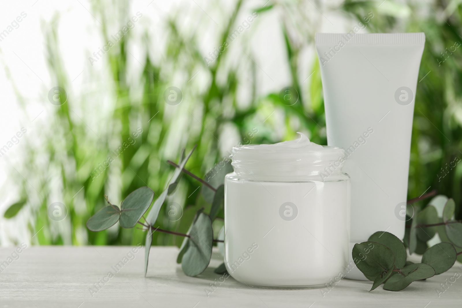 Photo of Different hand care cosmetic products and eucalyptus branches on white wooden table, space for text