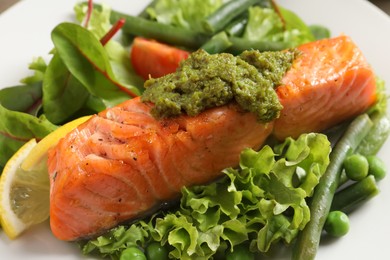 Photo of Tasty cooked salmon with pesto sauce and fresh salad on plate, closeup