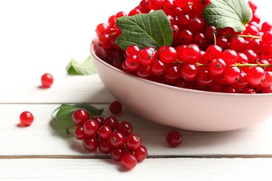 Photo of Delicious red currants and leaves on white wooden table, closeup