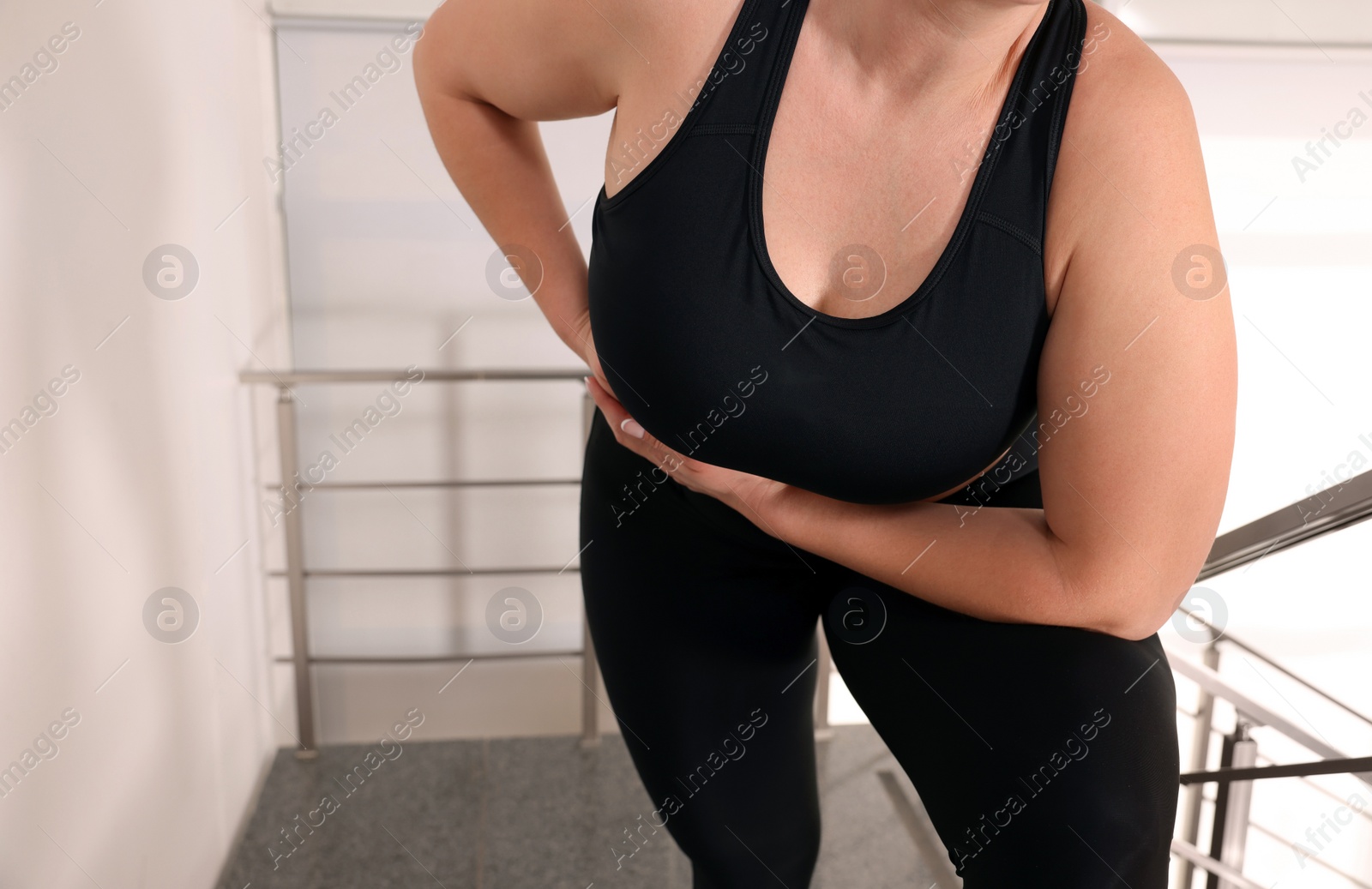 Photo of Overweight woman suffering from pain in right side on stairs indoors, closeup. Space for text