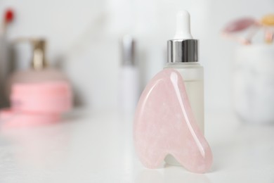 Photo of Rose quartz gua sha tool and cosmetic product on white table, closeup. Space for text