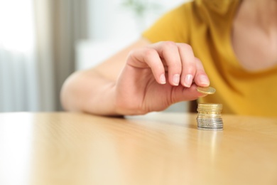Photo of Woman stacking coins on table at home, closeup. Space for text