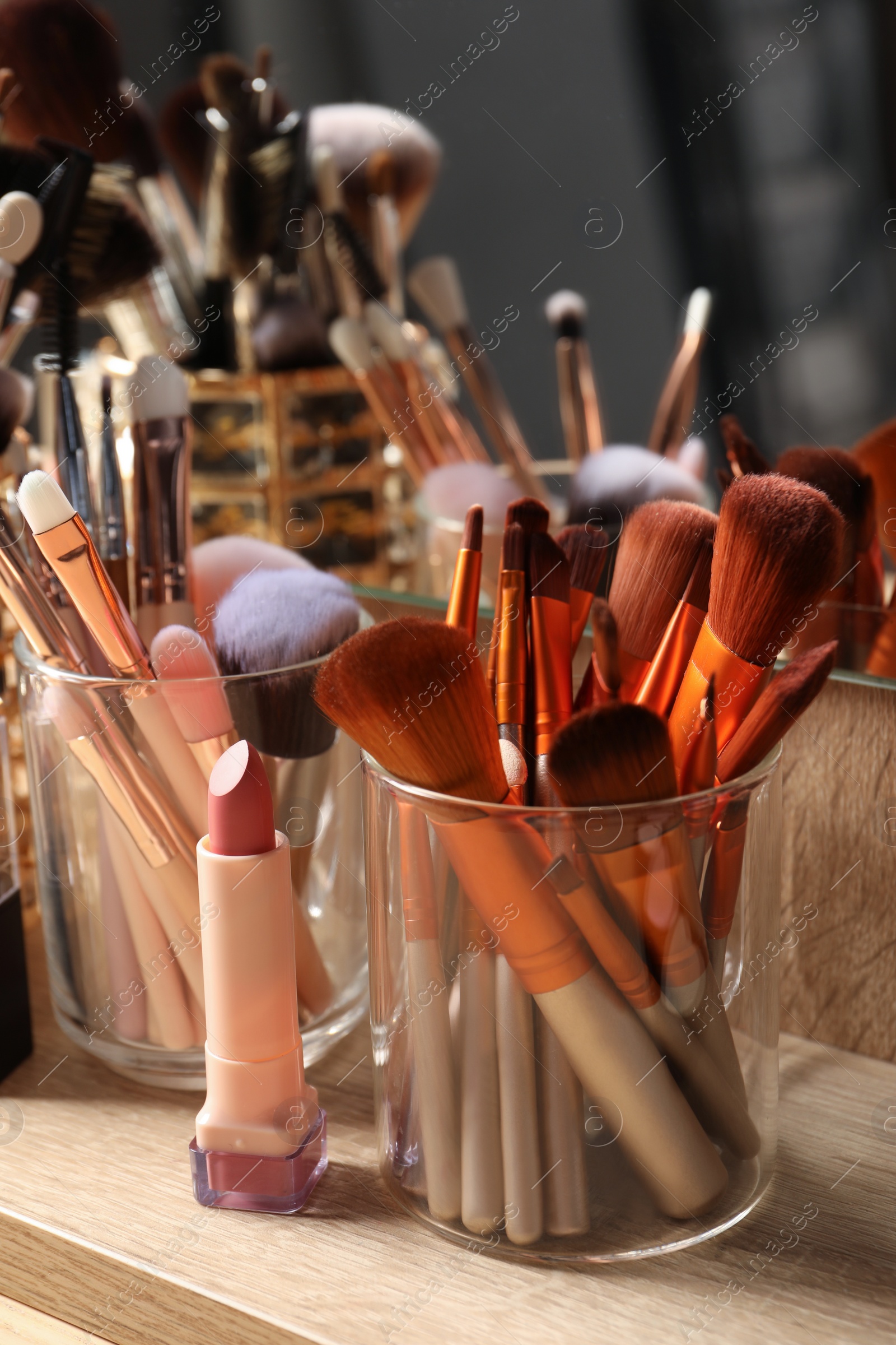 Photo of Set of professional brushes and makeup products near mirror on wooden table