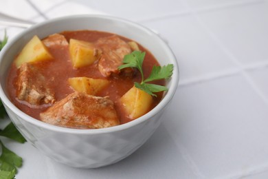 Photo of Delicious goulash in bowl on white tiled table, closeup. Space for text