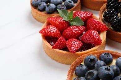 Photo of Tartlets with different fresh berries on white marble table, closeup. Delicious dessert