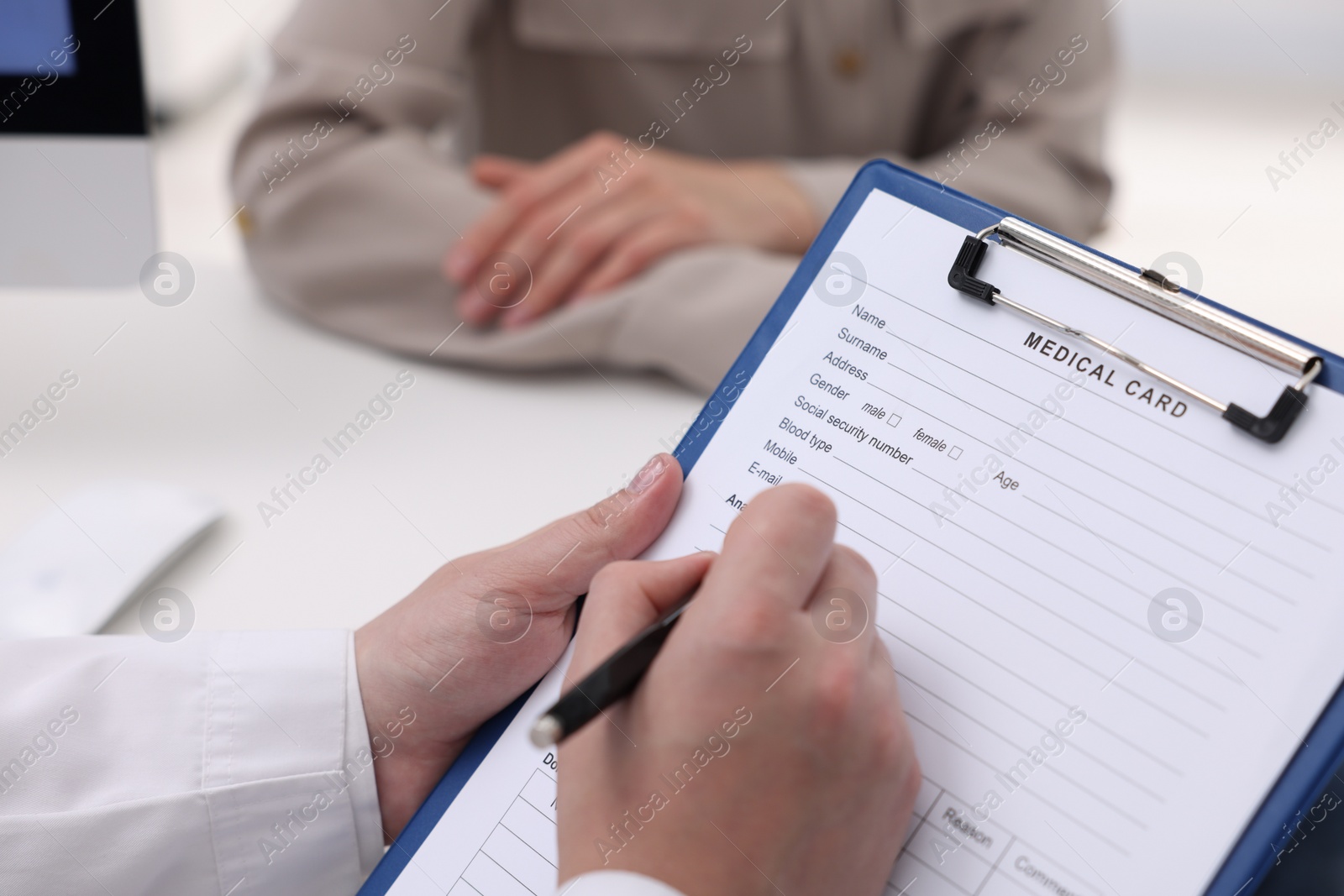 Photo of Doctor filling out patient's medical card at table in clinic, closeup