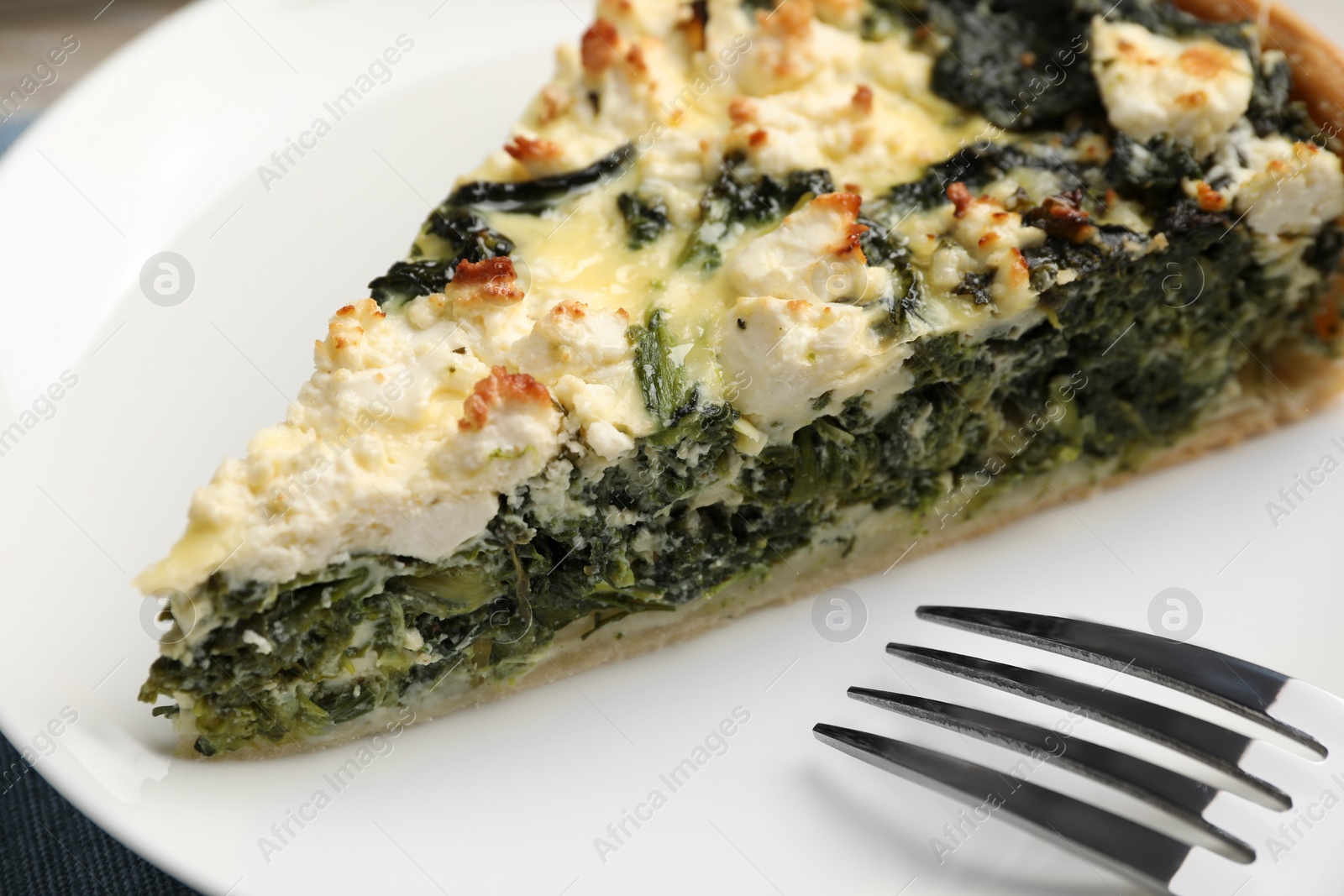 Photo of Piece of delicious homemade spinach quiche and fork on white plate, closeup