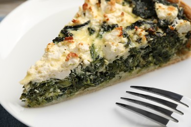 Piece of delicious homemade spinach quiche and fork on white plate, closeup