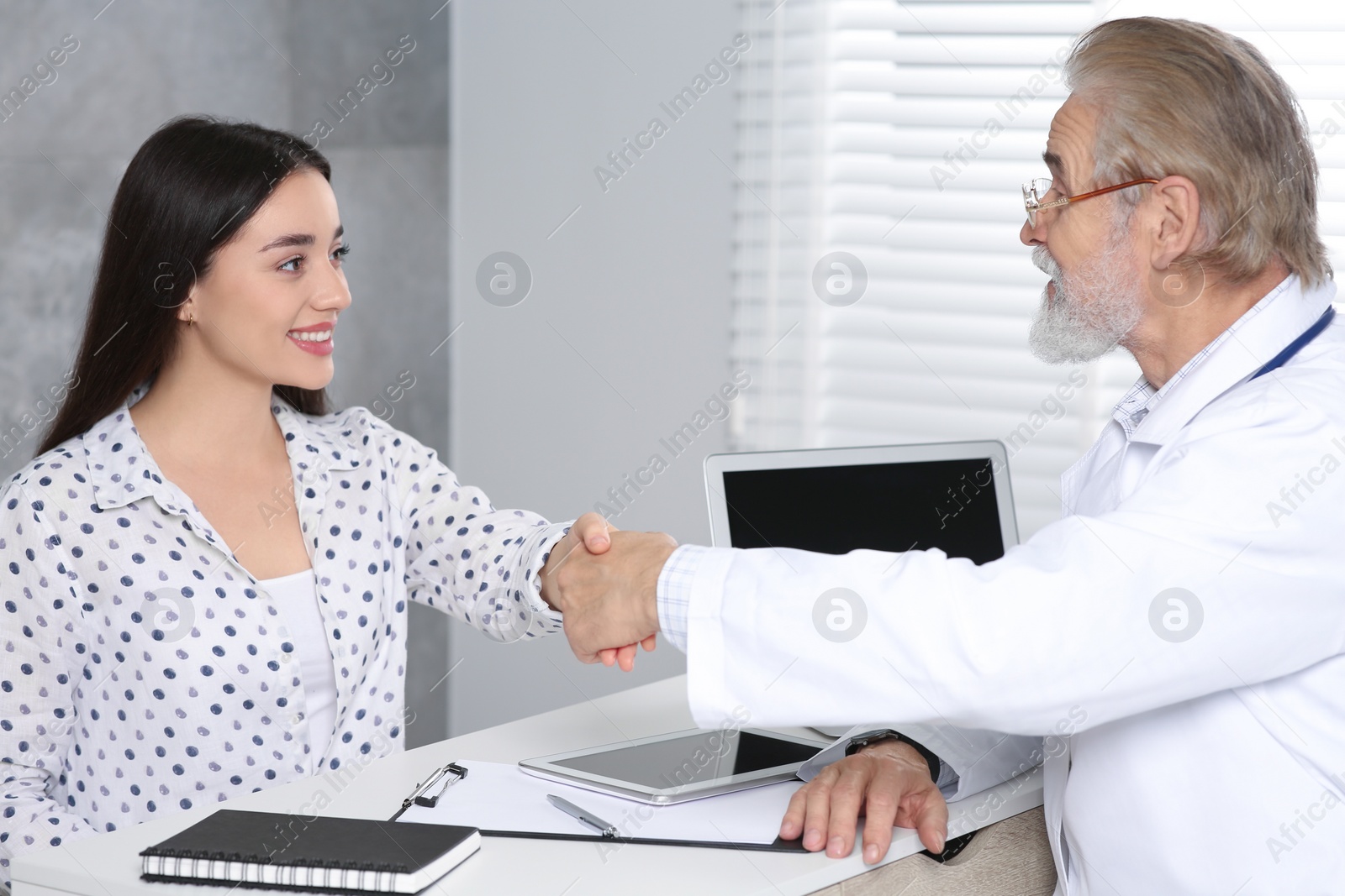 Photo of Happy senior doctor shaking hands with patient in clinic