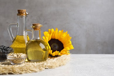 Photo of Sunflower cooking oil, seeds and yellow flowers on light grey table, space for text
