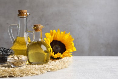 Sunflower cooking oil, seeds and yellow flowers on light grey table, space for text