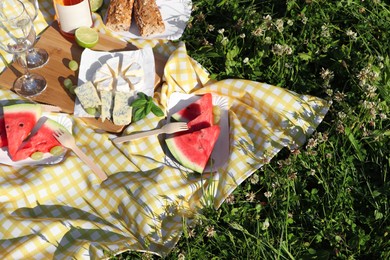 Photo of Picnic blanket with delicious food and wine on green grass outdoors, above view