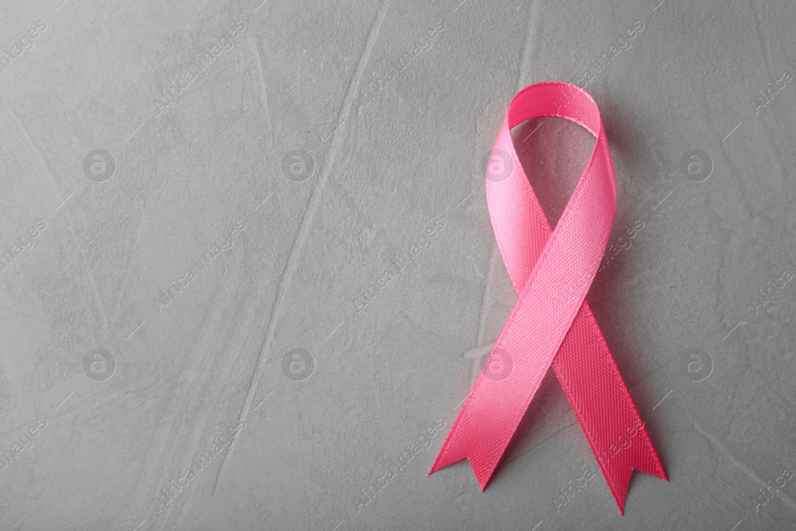 Photo of Pink ribbon on grey background, top view with space for text. Breast cancer awareness concept