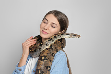 Young woman with boa constrictor on light background. Exotic pet