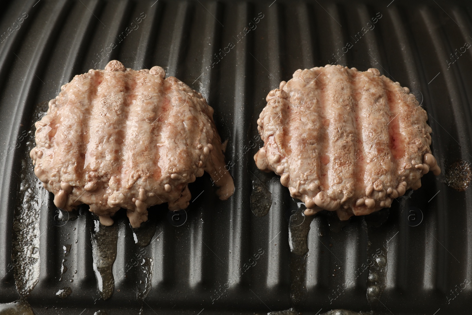 Photo of Delicious hamburger patties cooking on electric grill, closeup