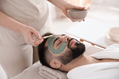 Photo of Cosmetologist applying mask on man's face in spa salon