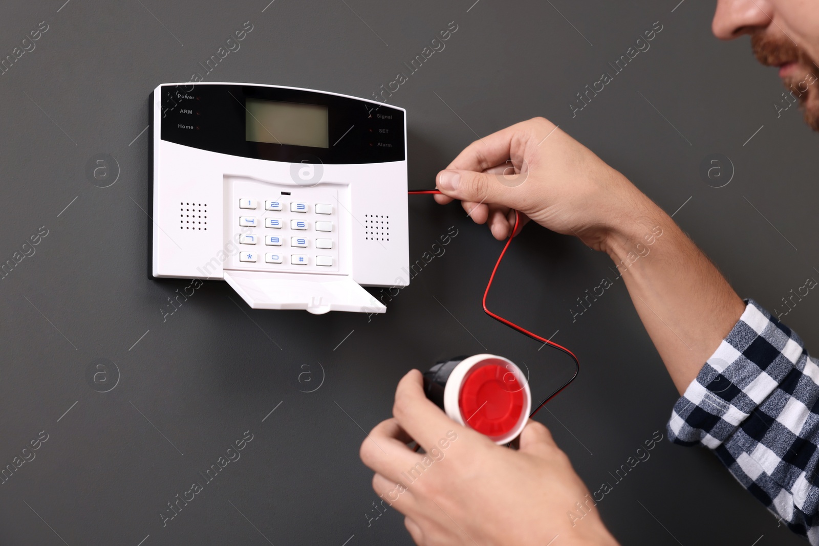 Photo of Man checking home security alarm system with mini horn siren near gray wall, closeup