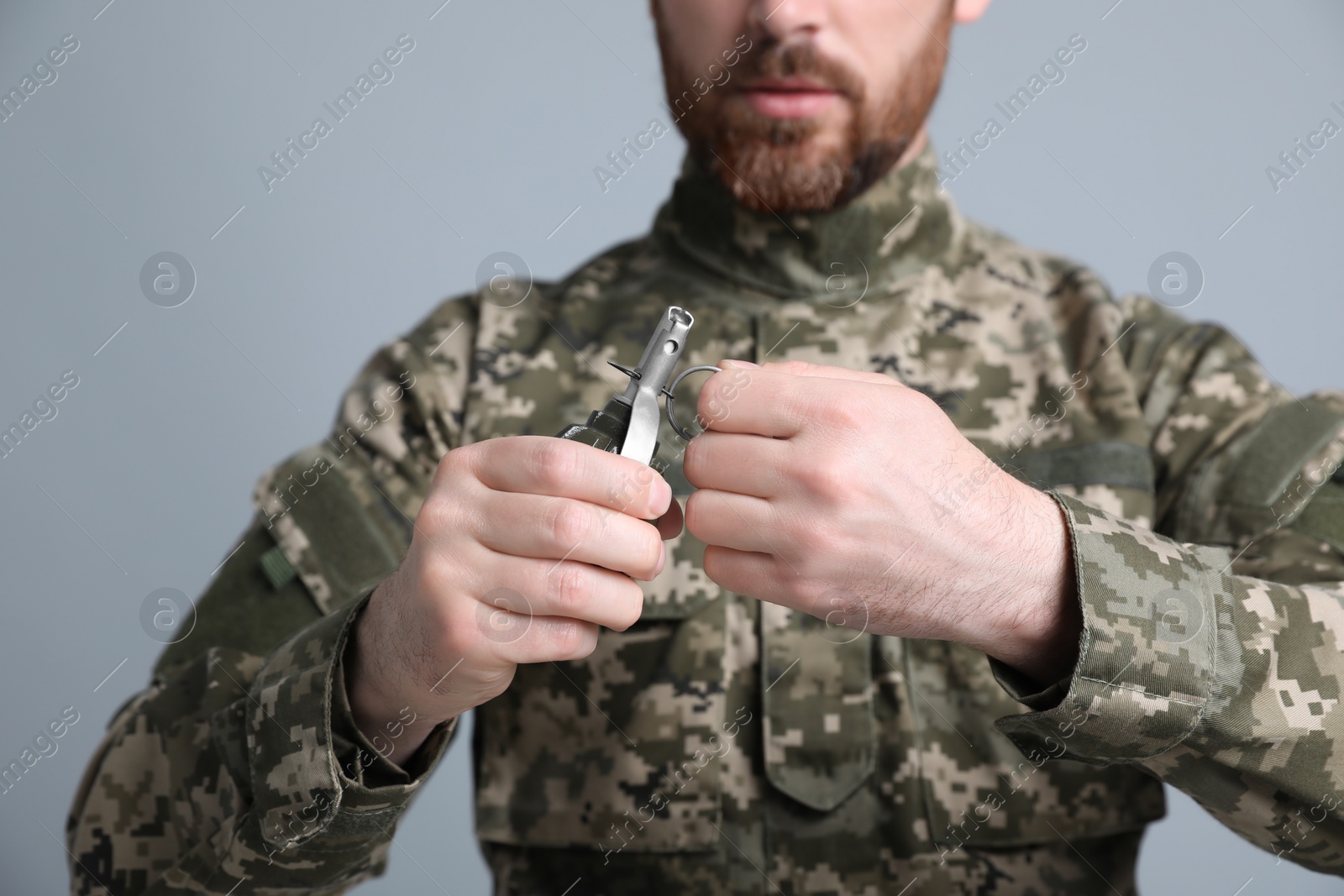 Photo of Soldier pulling safety pin out of hand grenade on light grey background, closeup. Military service